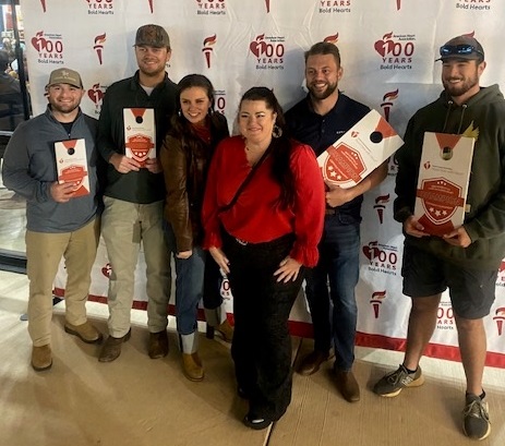 Group of six people holding awards standing in front of American Heart Association 100 years Bold Heart Banner.